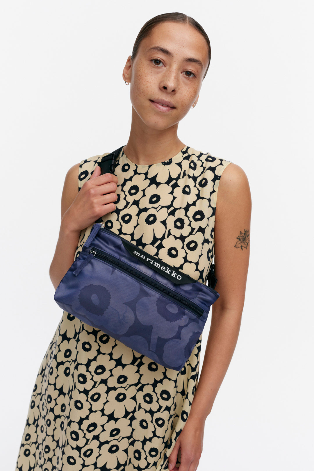 Woman holding a blue handbag with a floral dress against a white background