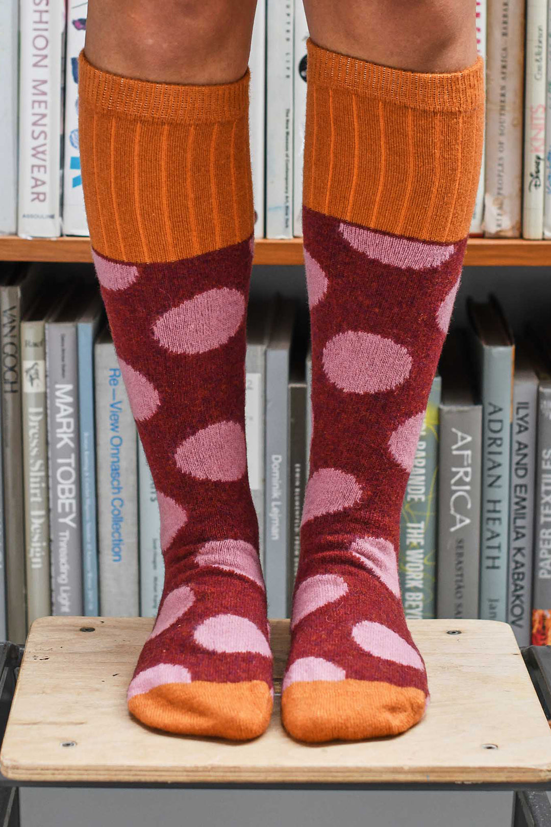 Person wearing orange knee-high socks with pink heart pattern on a bookshelf background