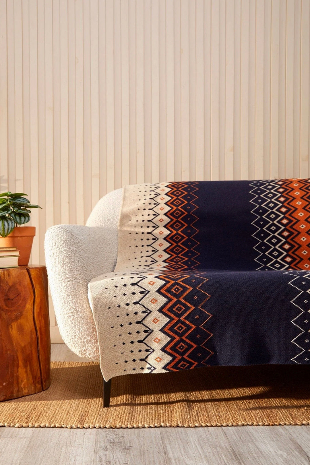 Patterned blanket draped over a white sofa against a striped wall.