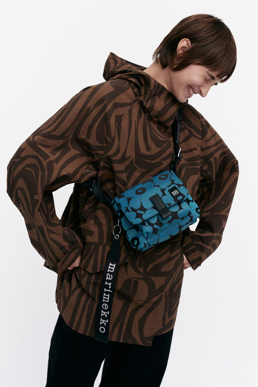 Person wearing a brown patterned jacket with a blue Marimekko bag on a white background