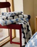 A stack of folded plush towels with a blue, white, and gray abstract dot pattern sits on a red wooden chair next to a window.