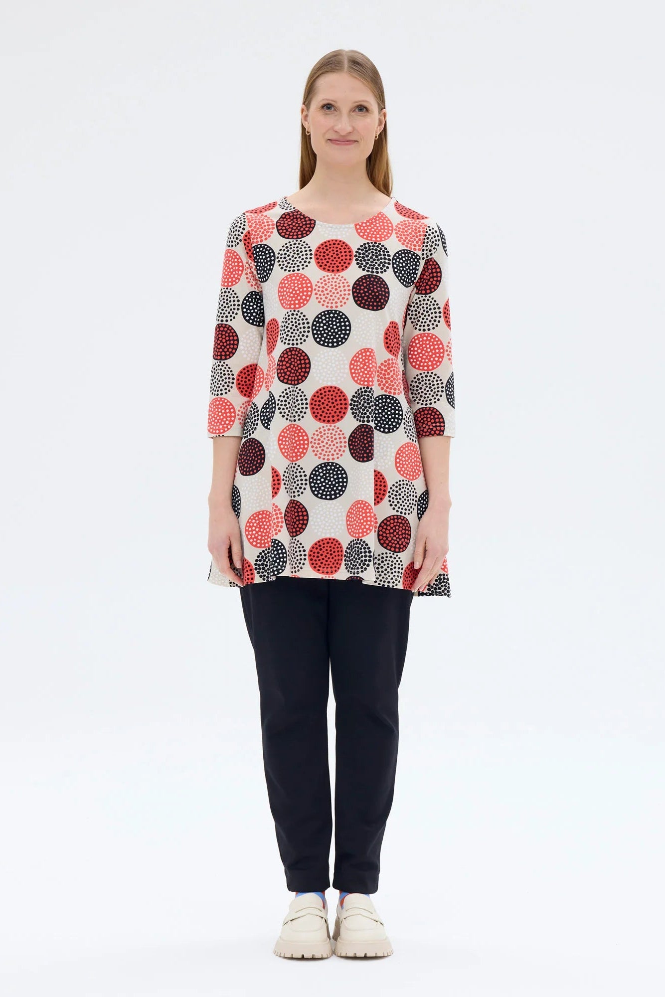 Woman wearing a patterned long-sleeve top and dark pants on a white background