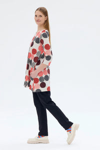 Woman wearing a colorful polka dot dress with black pants on a white background