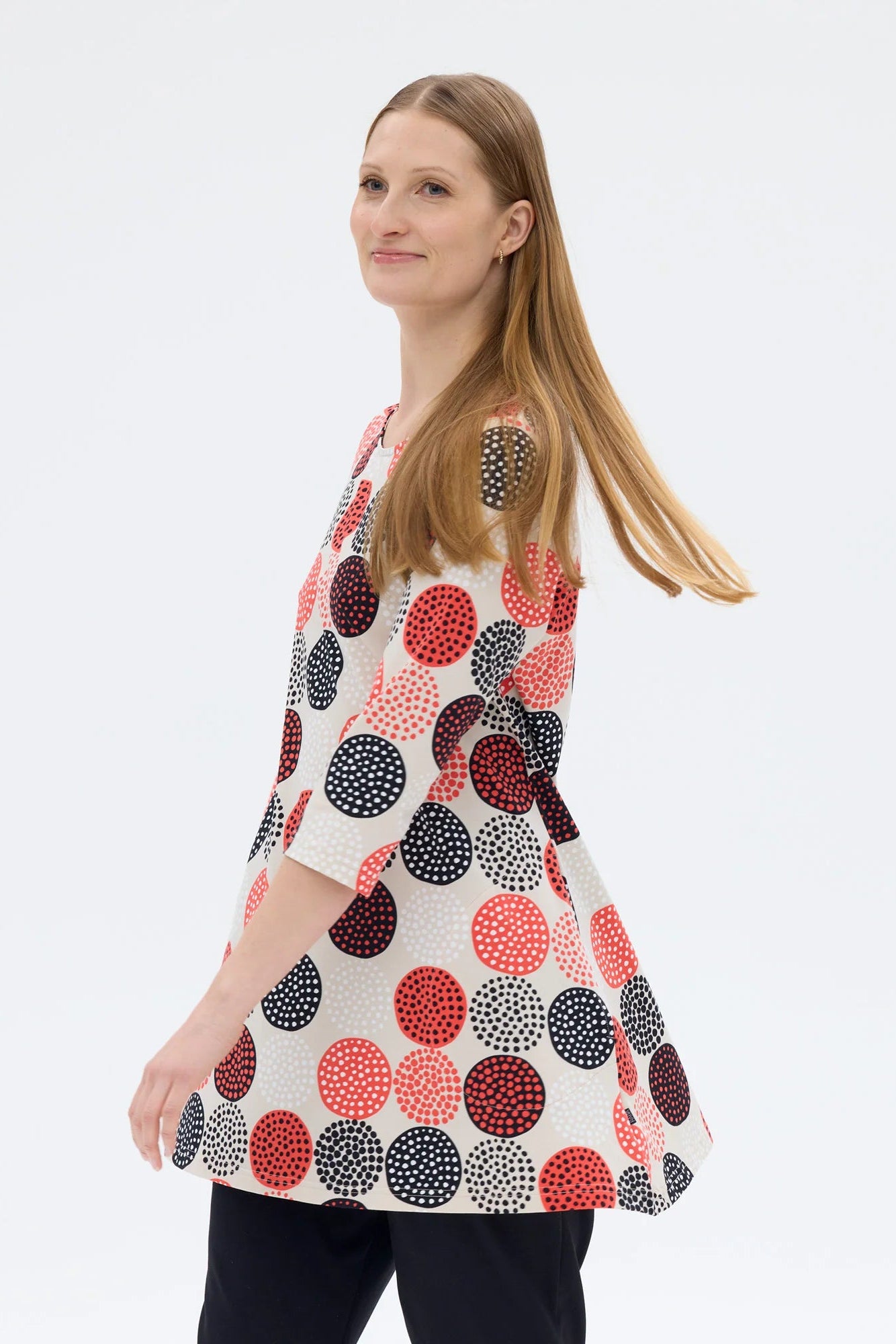 Woman wearing a patterned dress with red, black, and white circles on a plain background