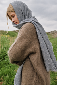 A woman outdoors wearing a soft taupe-brown fuzzy coat and a gray knit headscarf with small white embroidered floral motifs.