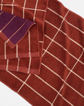 A close-up of folded towels showing a rust red and cream grid pattern, with one folded corner revealing a purple and rust striped inner side.