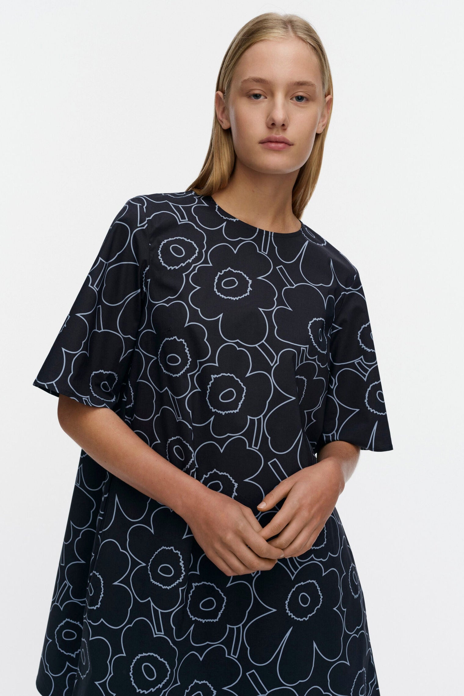 Woman wearing a blue dress with white floral pattern on a plain background