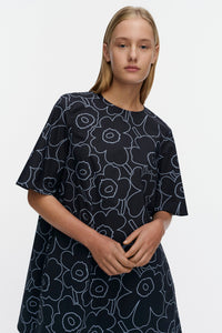 Woman wearing a blue dress with white floral pattern on a plain background