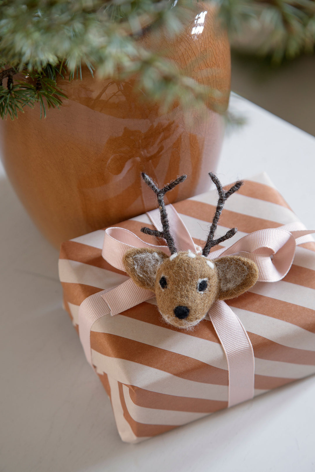 Small reindeer figurine on a striped gift box with a potted plant in the background
