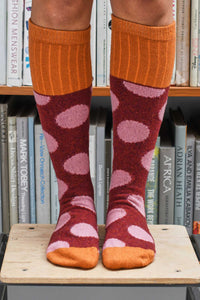 Person wearing orange knee-high socks with pink heart pattern on a bookshelf background