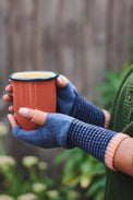 Person holding a terracotta cup with blue fingerless gloves in an outdoor setting