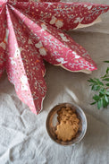 A red paper star with Moomin characters decoration, displayed above a bowl of cookies, with a floral pattern in the background.