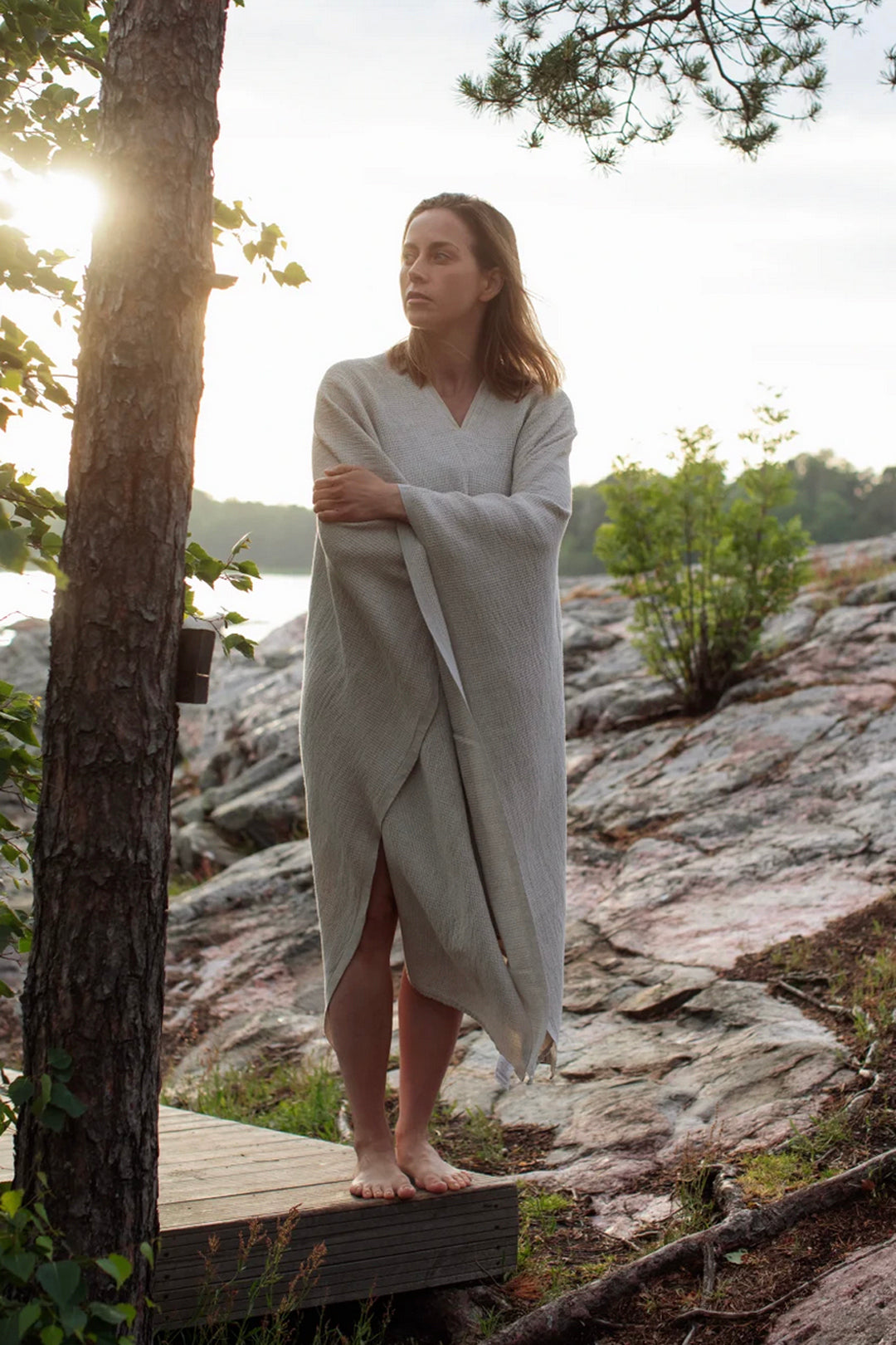 Woman wrapped in a light fabric standing on a rocky outcrop with a natural landscape in the background