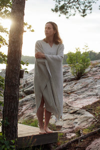 Woman wrapped in a light fabric standing on a rocky outcrop with a natural landscape in the background