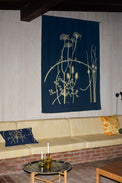 Navy tapestry with yellow floral design on a wall above a beige sofa with decorative pillows.